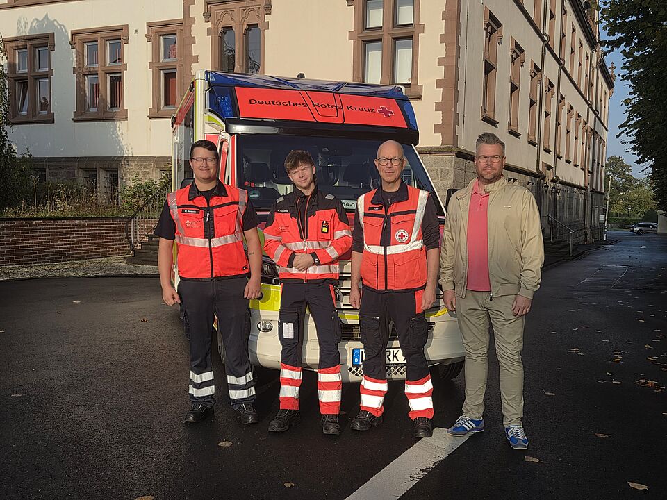 Vier Personen stehen vor einem Rettungswagen