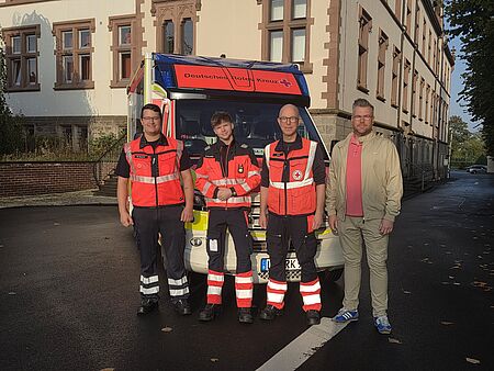 Vier Personen stehen vor einem Rettungswagen