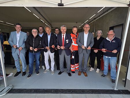 Sieben Herren durchschneiden mit einer Schere ein rotes Band. 