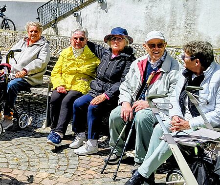 Vier Senioren sitzen auf einer Bank und freuen sich an der Gemeinschaft.