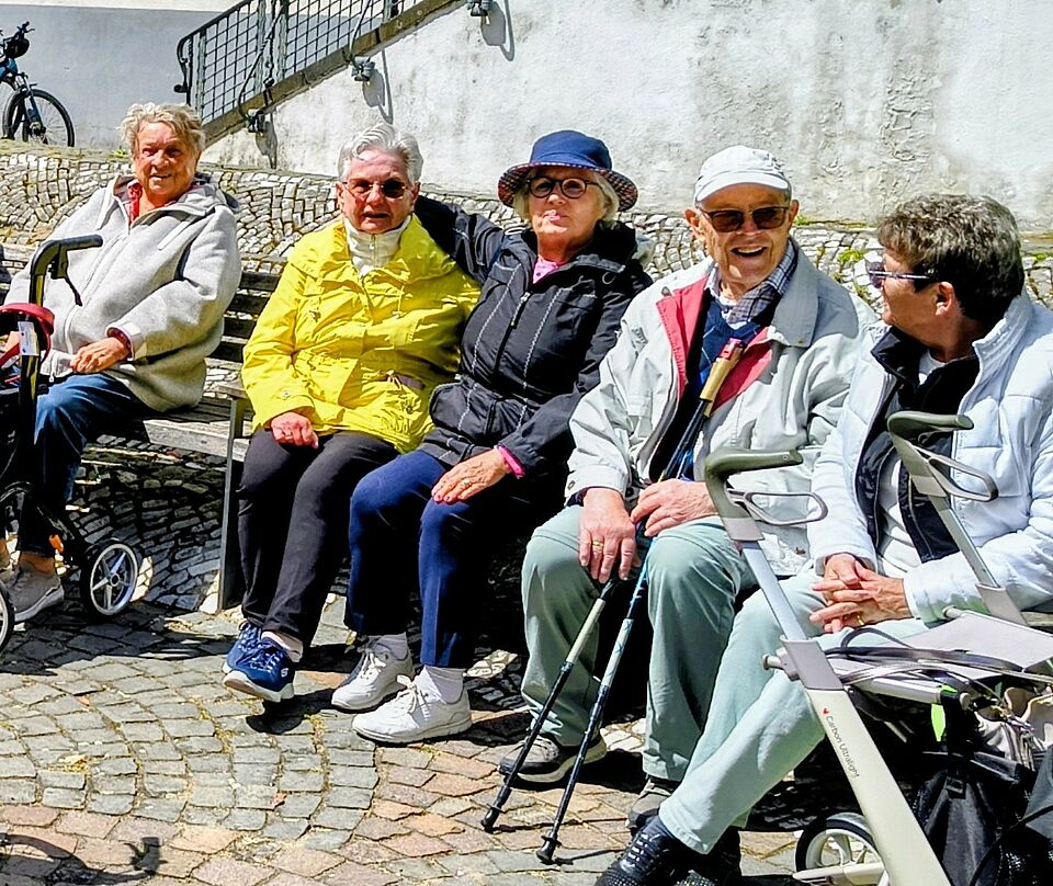 Vier Senioren sitzen auf einer Bank und freuen sich an der Gemeinschaft.